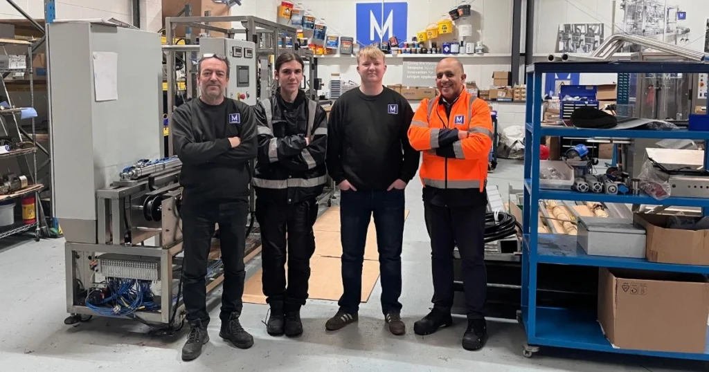 The Mount Filling Systems engineering and production team standing in the Dewsbury workshop with filling machinery in the background.