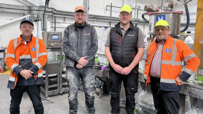 Mount Filling Systems and Tor Coatings team members standing beside industrial paint filling machinery